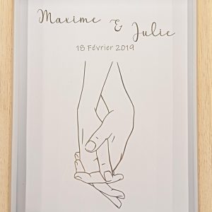 cadre en bois avec deux mains homme et femme qui se tiennent par la main. au dessus les deux prénoms des personnes avec leur date de rencontre ou mariage.