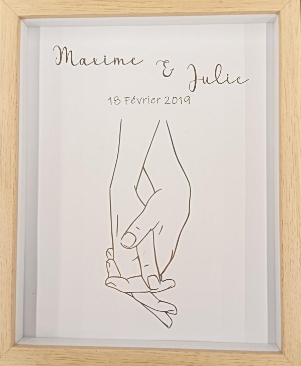 cadre en bois avec deux mains homme et femme qui se tiennent par la main. au dessus les deux prénoms des personnes avec leur date de rencontre ou mariage.