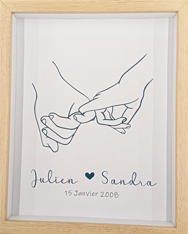 cadre en bois effet 3D avec une image de deux mains homme et femme qui se tiennent par les petits doigts. en dessous sont écrits les prénoms des deux personnes avec un coeur entre les deux et la date de rencontre ou mariage. effet doré