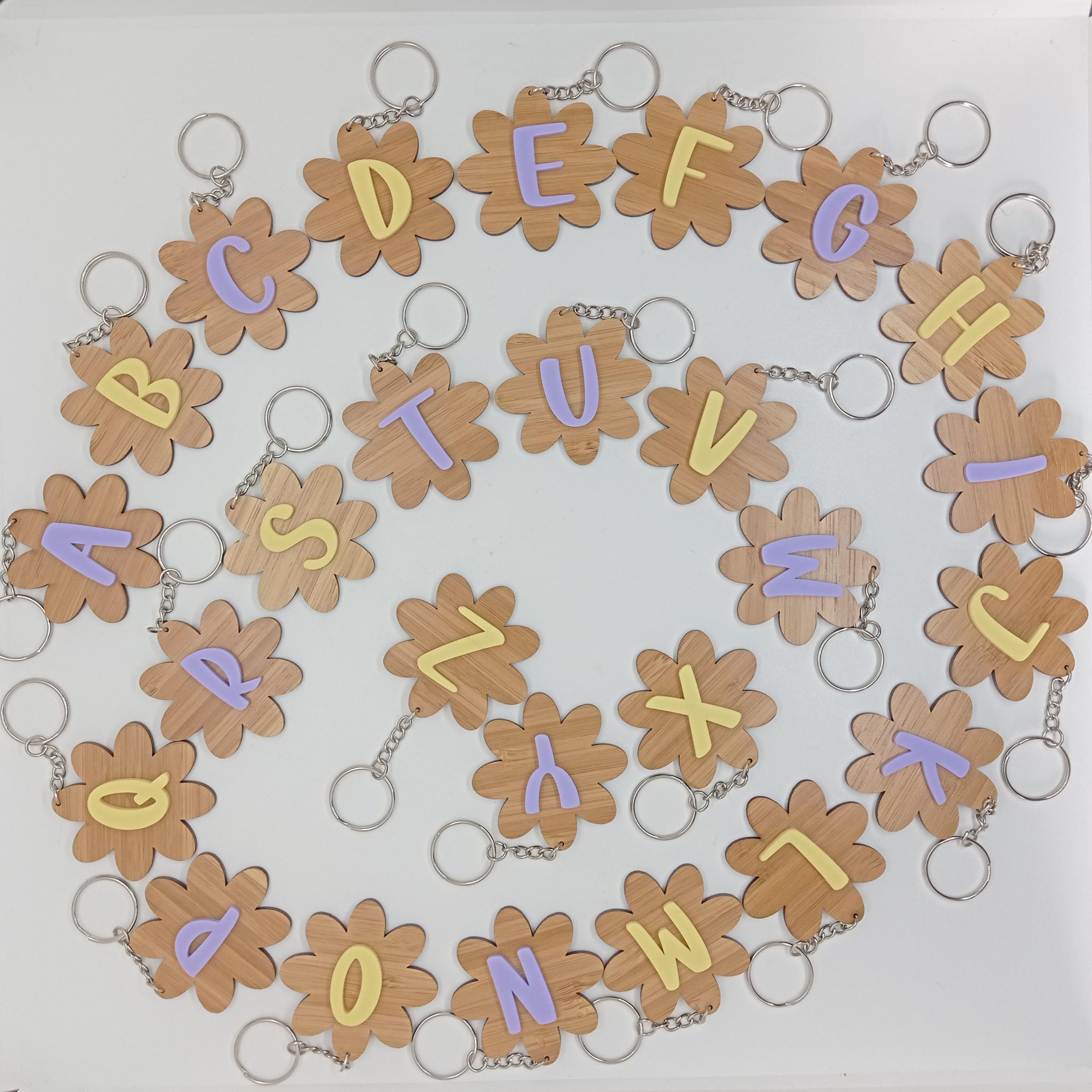 portes clés en bambou découpés en forme de fleurs avec une initiale collée dessus de couleur jaune ou violet pastel.